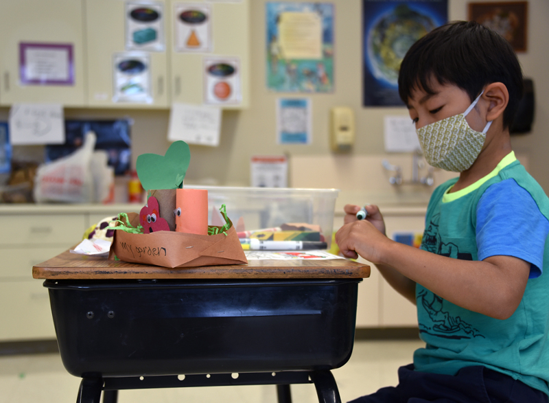 An Elisabeth Morrow School student sits at a desk with craft supplies while wearing a mask.