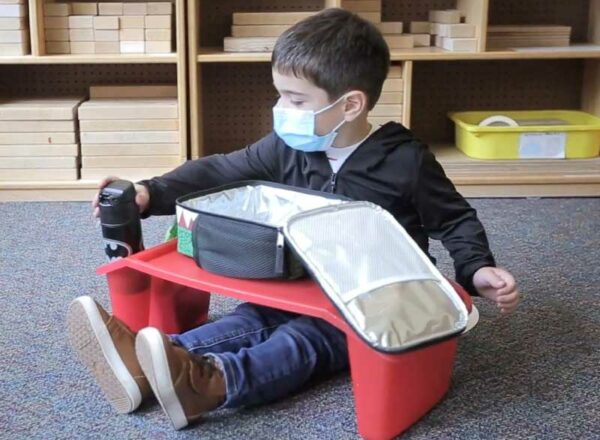 An Elisabeth Morrow School student opens a lunchbox while wearing a mask and using their own lapdesk.