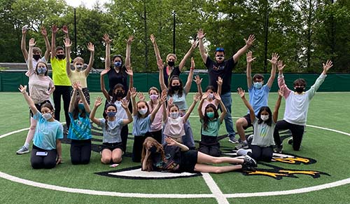 Group of people outside on sports field raising arms to sky