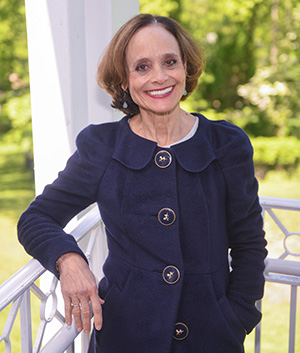 Maureen Fonseca, a smiling caucasian woman with light brown hair, wearing a dark blue suit with large buttons