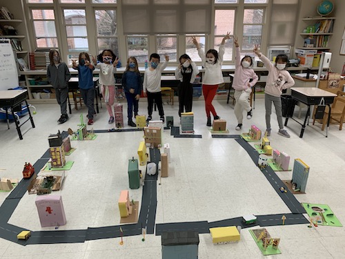 first-grade students cheering while standing behind the kid town they've built