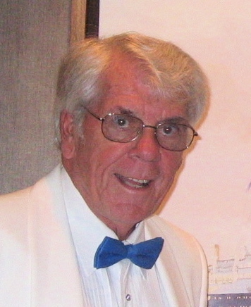 Smiling elderly caucasian gentleman with white hair and glasses, wearing a white suit and a blue bow tie