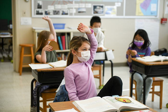 A young blonde girl wearing a mask in a schoolroom with other students at Elisabeth Morrow School
