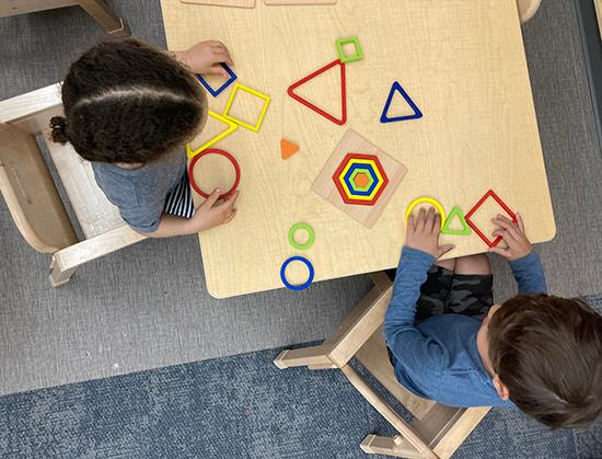 Seedlings Program at Elisabeth Morrow School, two small children shown from overhead working at a table on geometry toys.