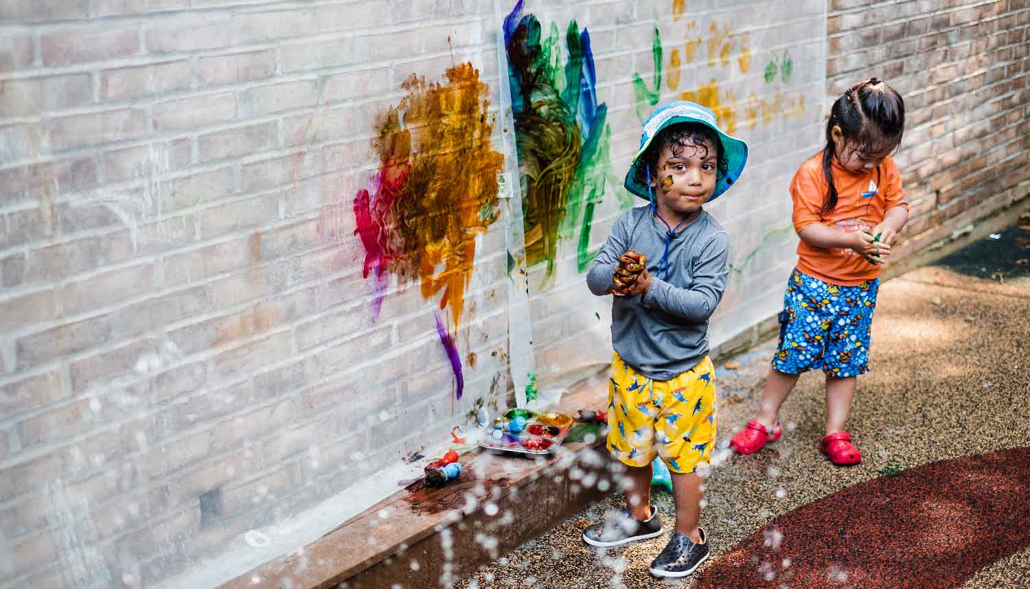 Summer Explorations young student painting on the brick wall