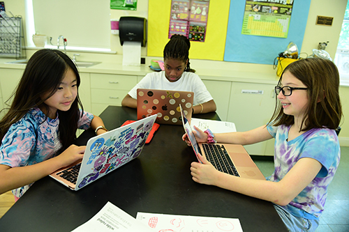 three students at a shared table looking at laptops