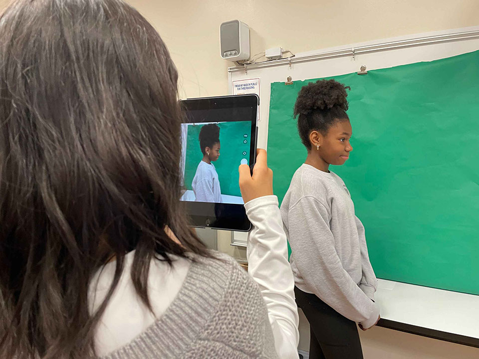 Students using iPad against a green screen.