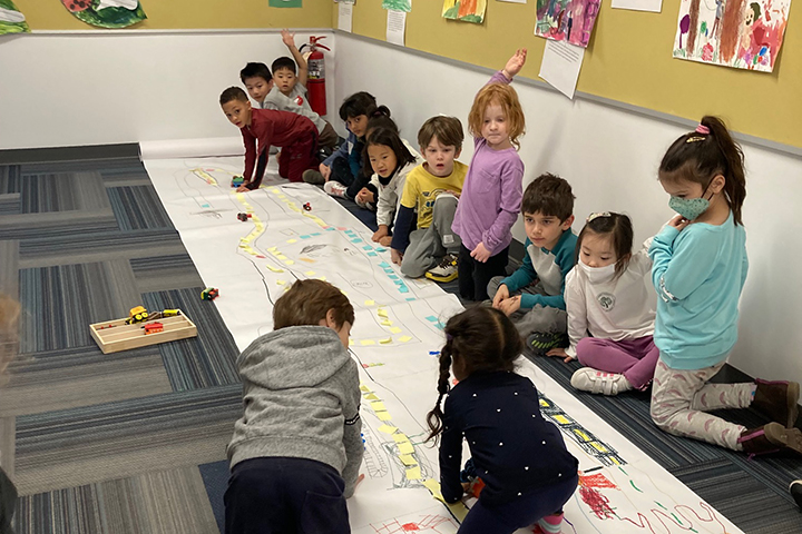 A 2s student drives a car down a drawn network 
of roads and towns designed by our Kindergarten students.