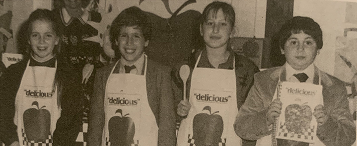 Student posting in delicious cookbook aprons, circa 1980s.
