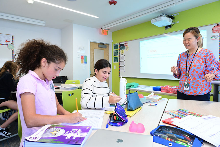 A teacher helps two middle school students in Morrow House with their math problems during class.