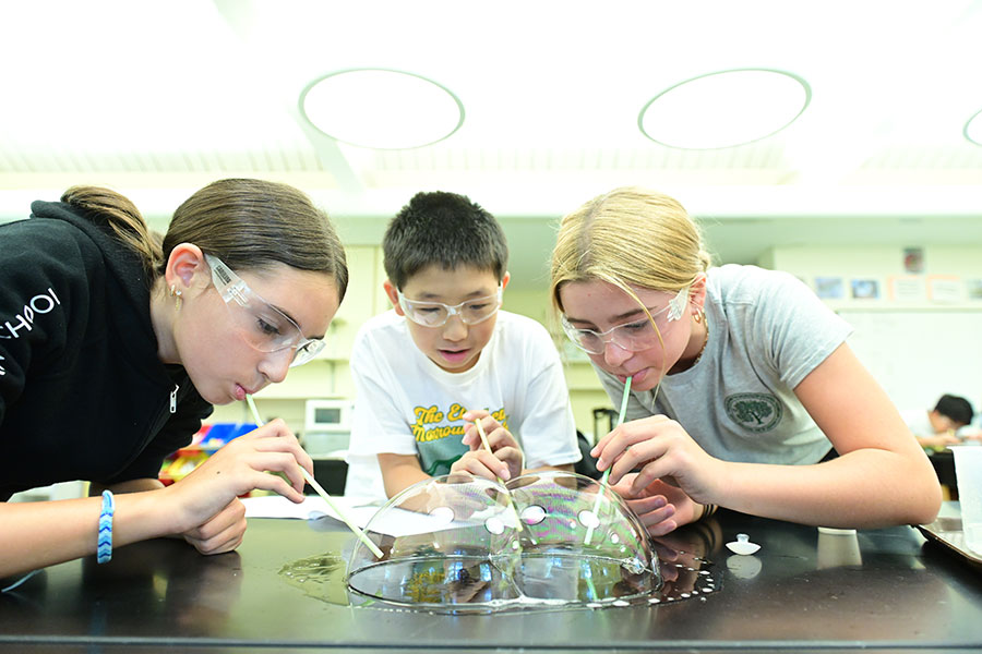 Three middle school students participating in a fun science experiment involving bubbles.