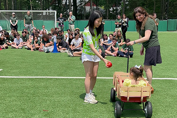 Oldest student passing apple to youngest student during an outdoor assembly.