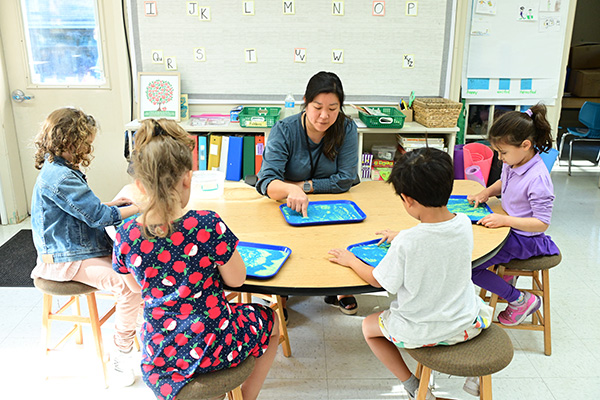 A Little School teacher helping first-grade students trace letters of the alphabet.